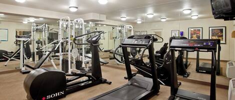 Une salle de sport équipée de divers appareils d’exercice, notamment des tapis de course, une machine de musculation et un vélo d’appartement.