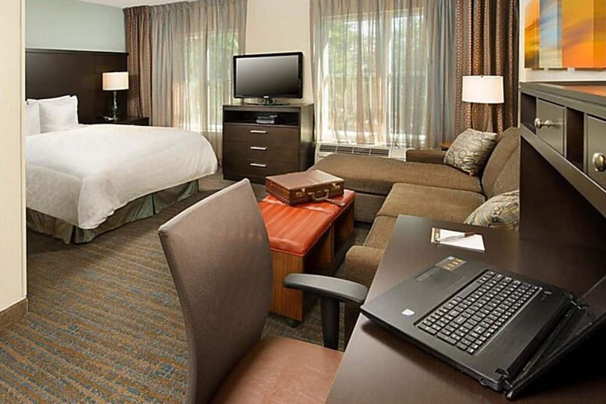 A hotel room with a bed, a desk with a laptop, a sofa, a TV, and a dresser.