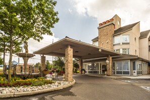 A hotel entrance with a covered patio, a fountain, and a landscaped garden.