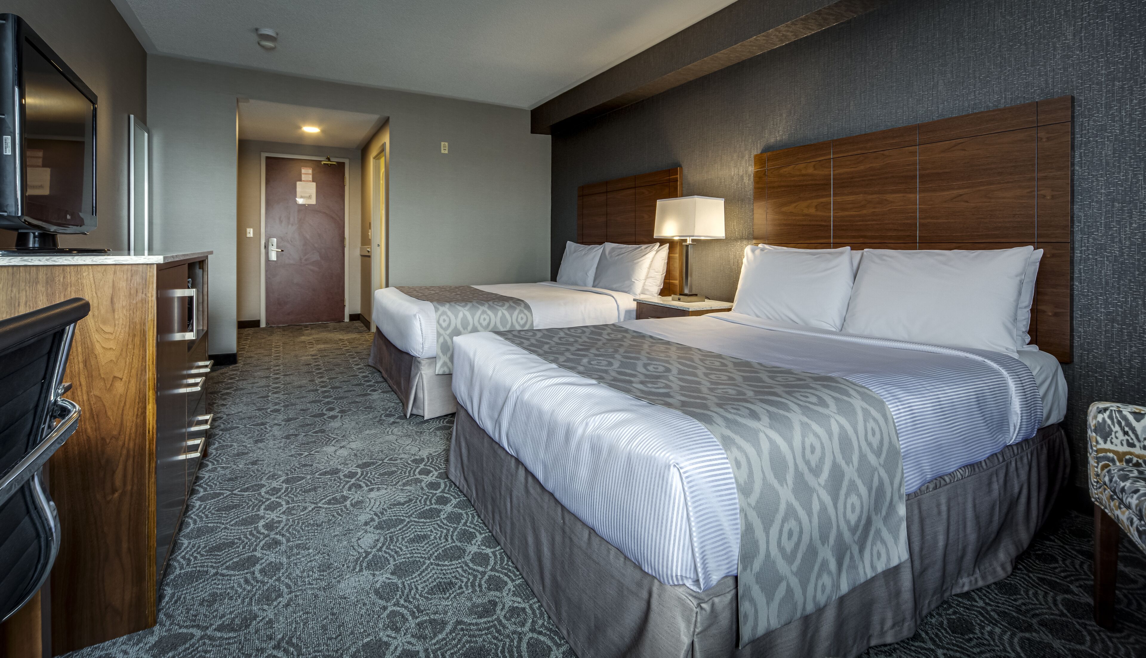 A hotel room with two beds, a desk, a TV, and a door leading to another room.
