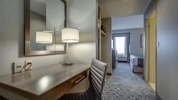 A hotel room with a wooden desk, two bedside lamps, a mirror, a chair, and a patterned carpet.