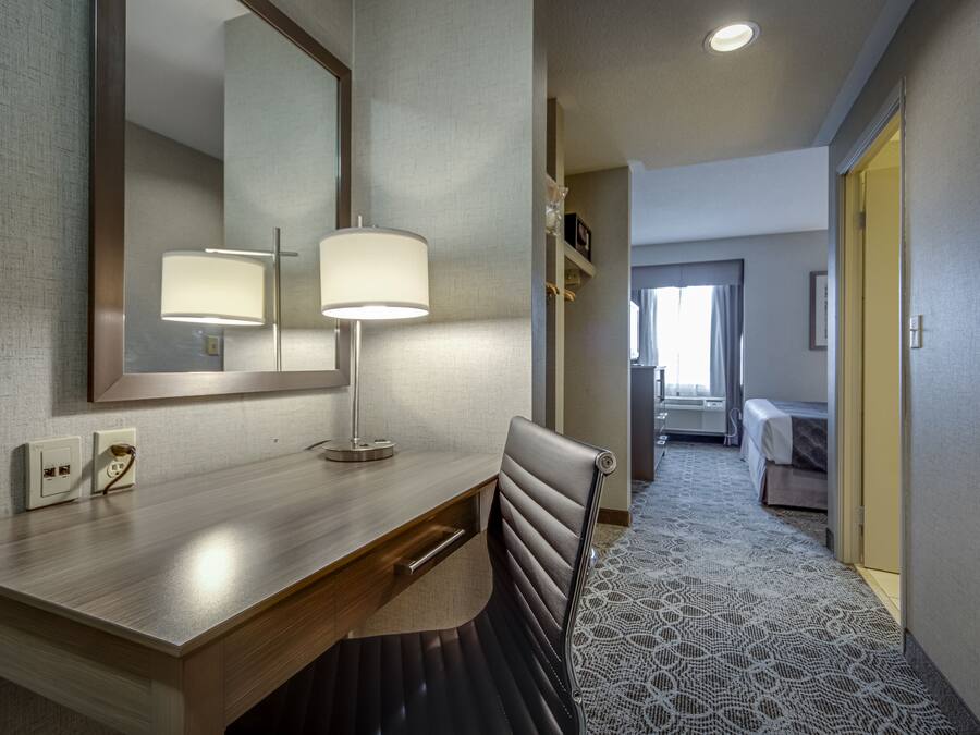 A hotel room with a wooden desk, two bedside lamps, a mirror, a chair, and a patterned carpet.