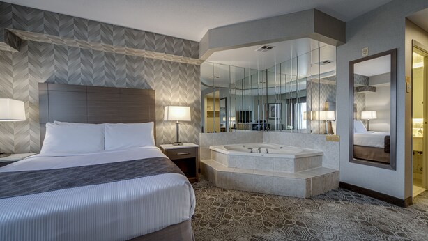 A hotel room with a large bed, a separate bathroom with a bathtub, and a large mirror.