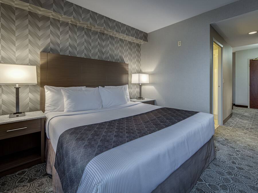A hotel room with a large bed, two bedside lamps, a wooden headboard, and a patterned carpet.