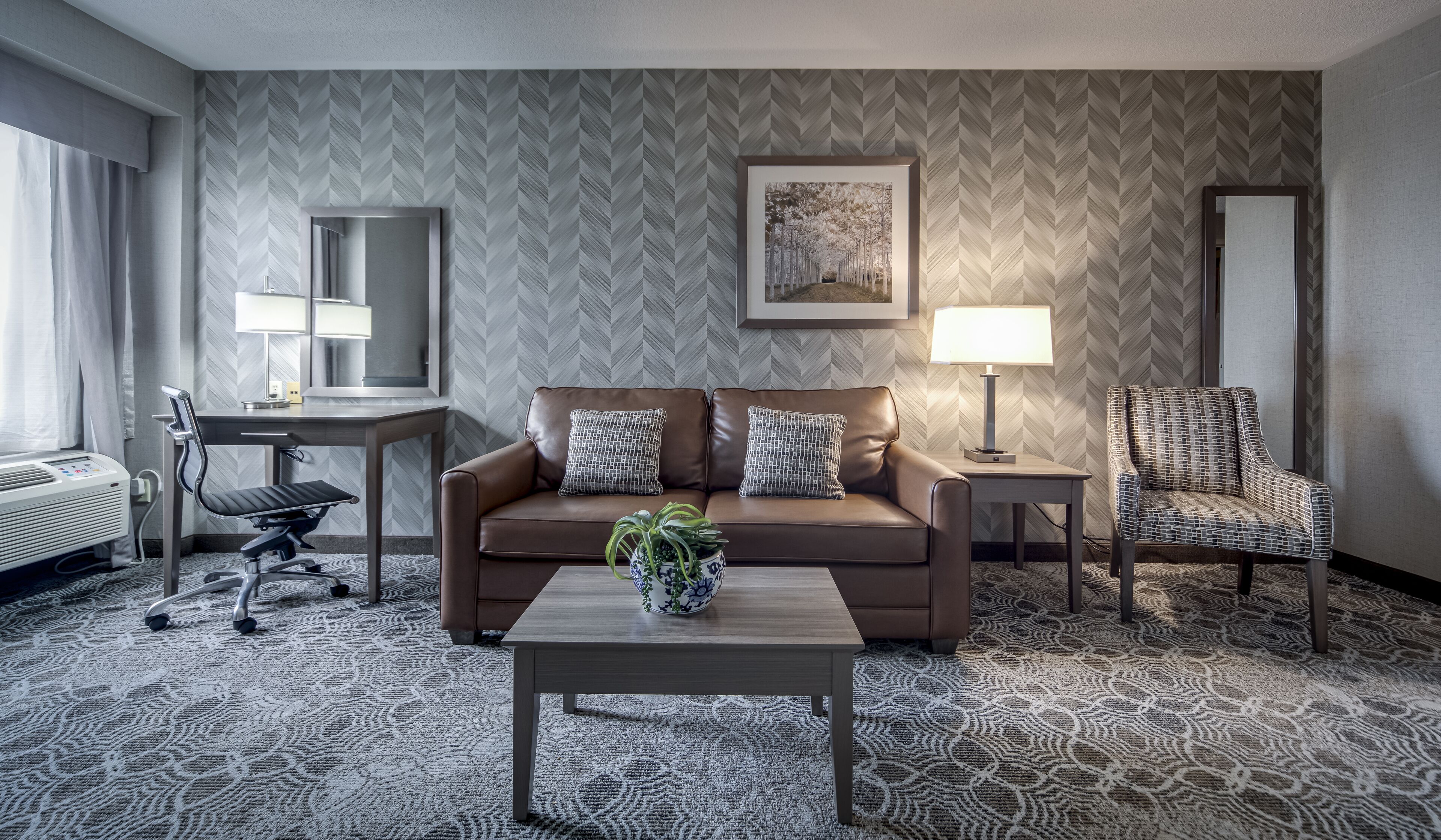 Habitación de hotel con sofá, sillón, escritorio y una mesa de centro con una planta.