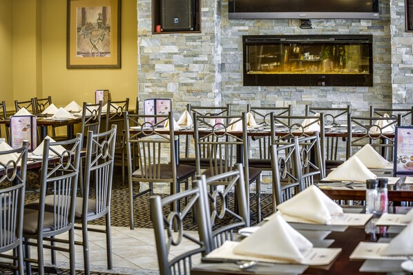 A restaurant with stone walls, metal chairs, and tables set with white napkins and menus.