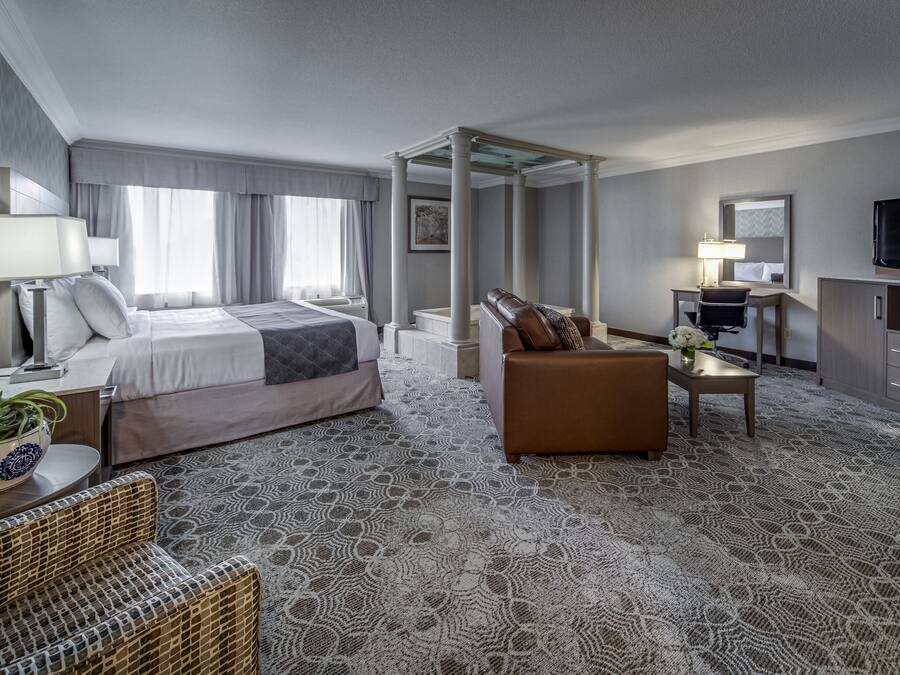 Una habitación de hotel con una cama grande, una zona de estar con sofá y sillón, televisión, escritorio con lámpara y microondas.