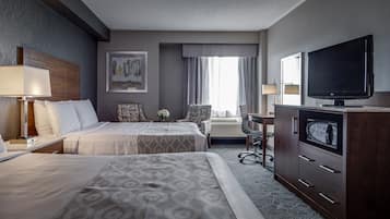 A hotel room with two beds, a desk, a television, and a large window with curtains.