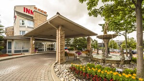 A hotel entrance with a covered patio, a fountain, and flower beds.