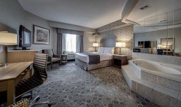 A hotel room with a bed, a desk, a chair, a TV, a lamp, a mirror, and a bathtub.