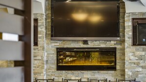 A restaurant with a stone wall, a large flat-screen TV, and multiple tables and chairs.