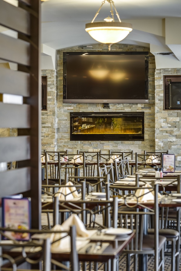 A restaurant with a stone wall, a large flat-screen TV, and multiple tables and chairs.
