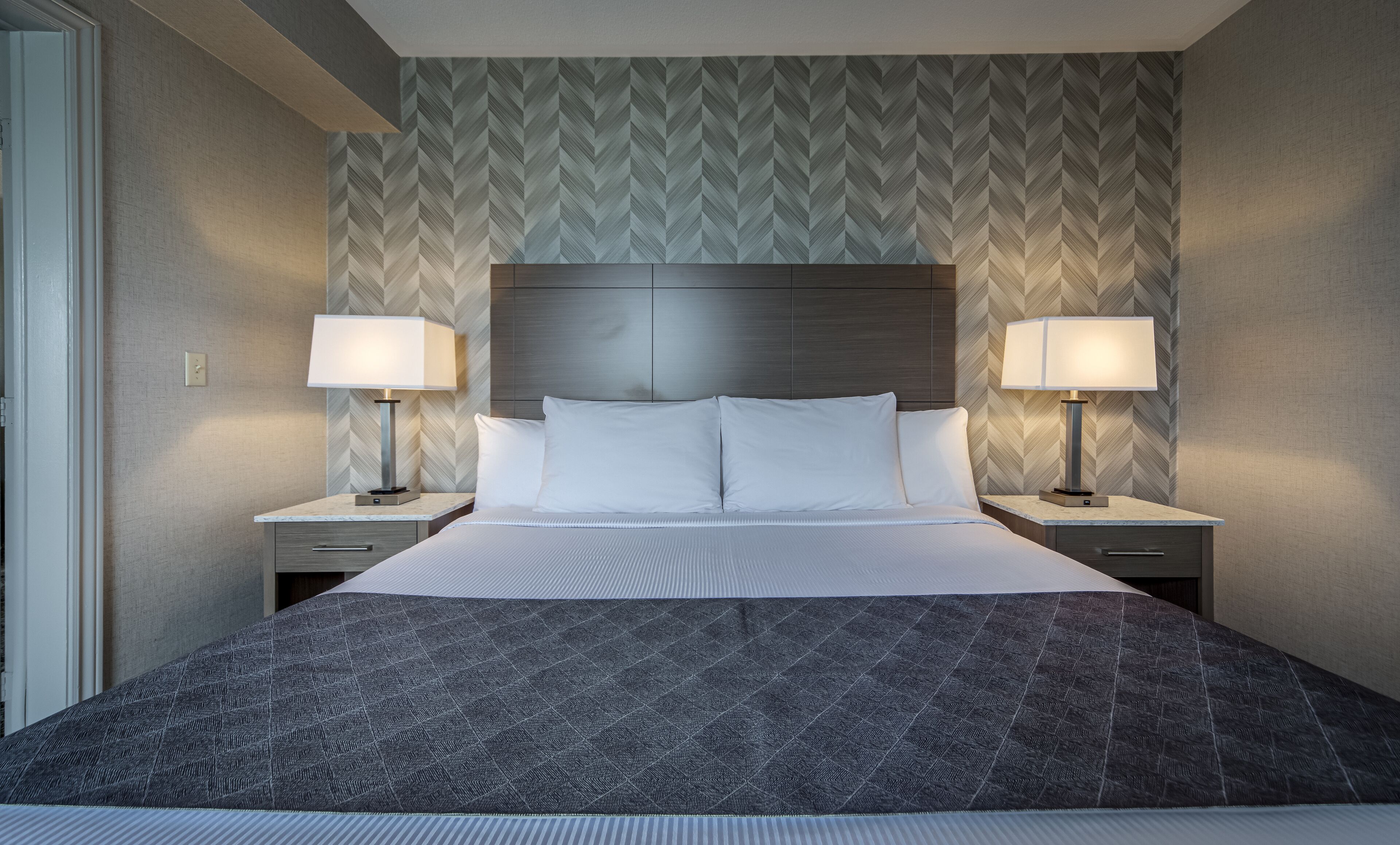 A hotel room with a large bed, two bedside tables, and a patterned wallpaper.