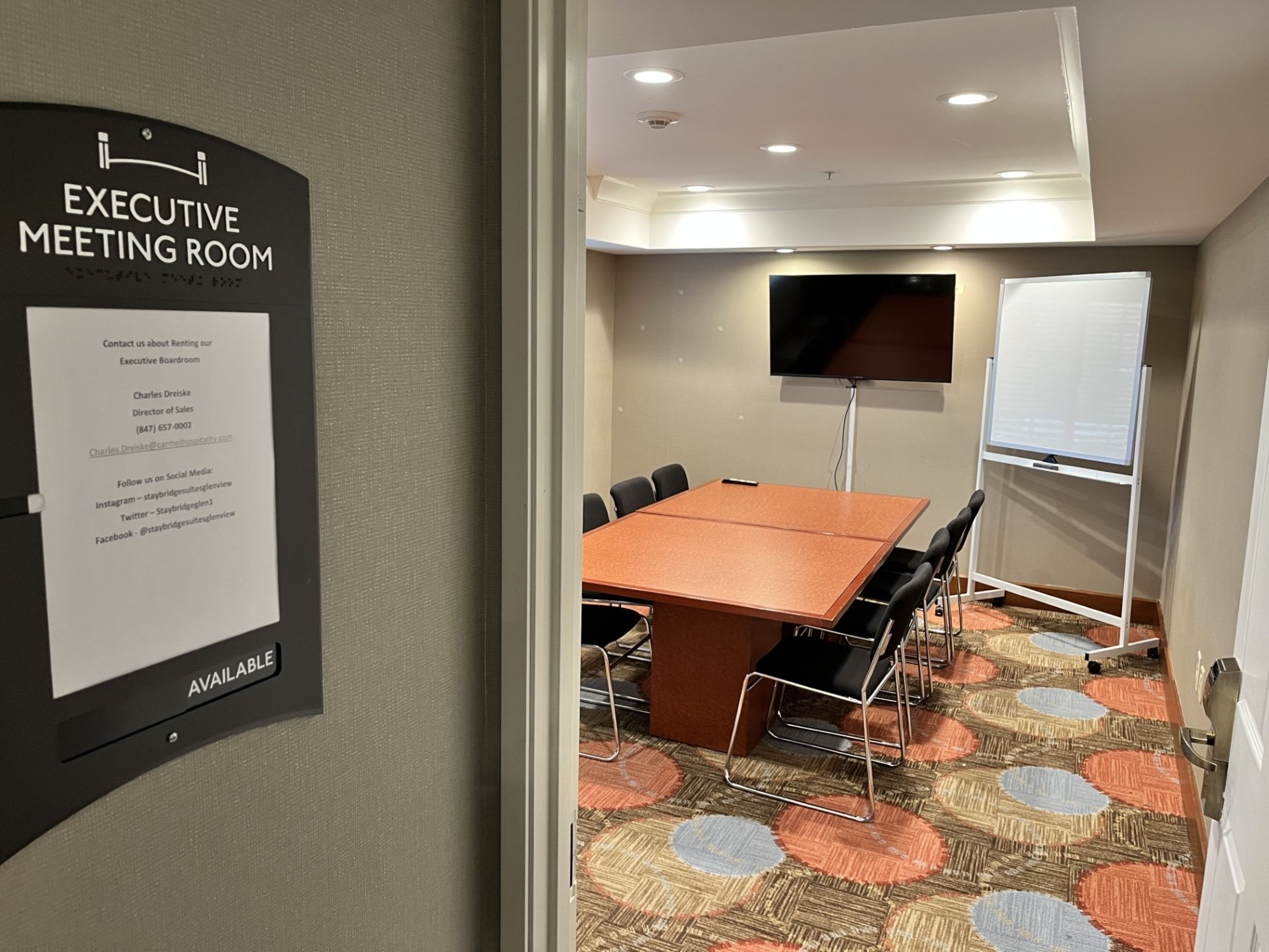 Un salón de conferencias con una mesa, sillas, una pizarra y un televisor.