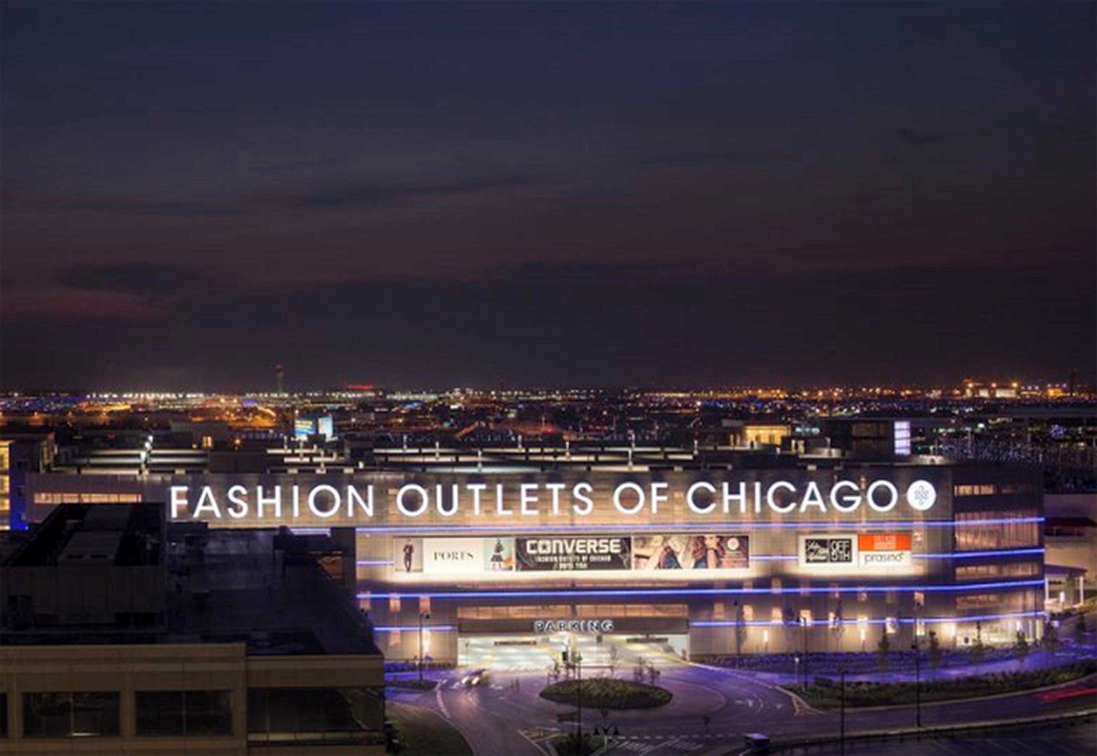 A multi-level shopping center with illuminated signage for various fashion outlets.