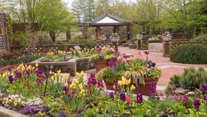 Un jardin agrémenté d’un belvédère, de différents parterres de fleurs et d’un chemin en briques.