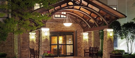Entrada de un hotel con un patio cubierto, paredes de piedra y mobiliario exterior.