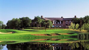 A golf course with a pond reflecting a building with multiple windows and a brick facade. - Staybridge Suites Chicago - Glenview by IHG (Glenview)