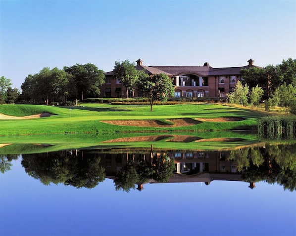 A golf course with a pond reflecting a building with multiple windows and a brick facade. - Staybridge Suites Chicago - Glenview by IHG (Glenview)