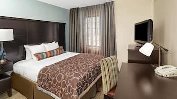 A hotel room with a large bed, a desk with a telephone, a television, and a lamp.