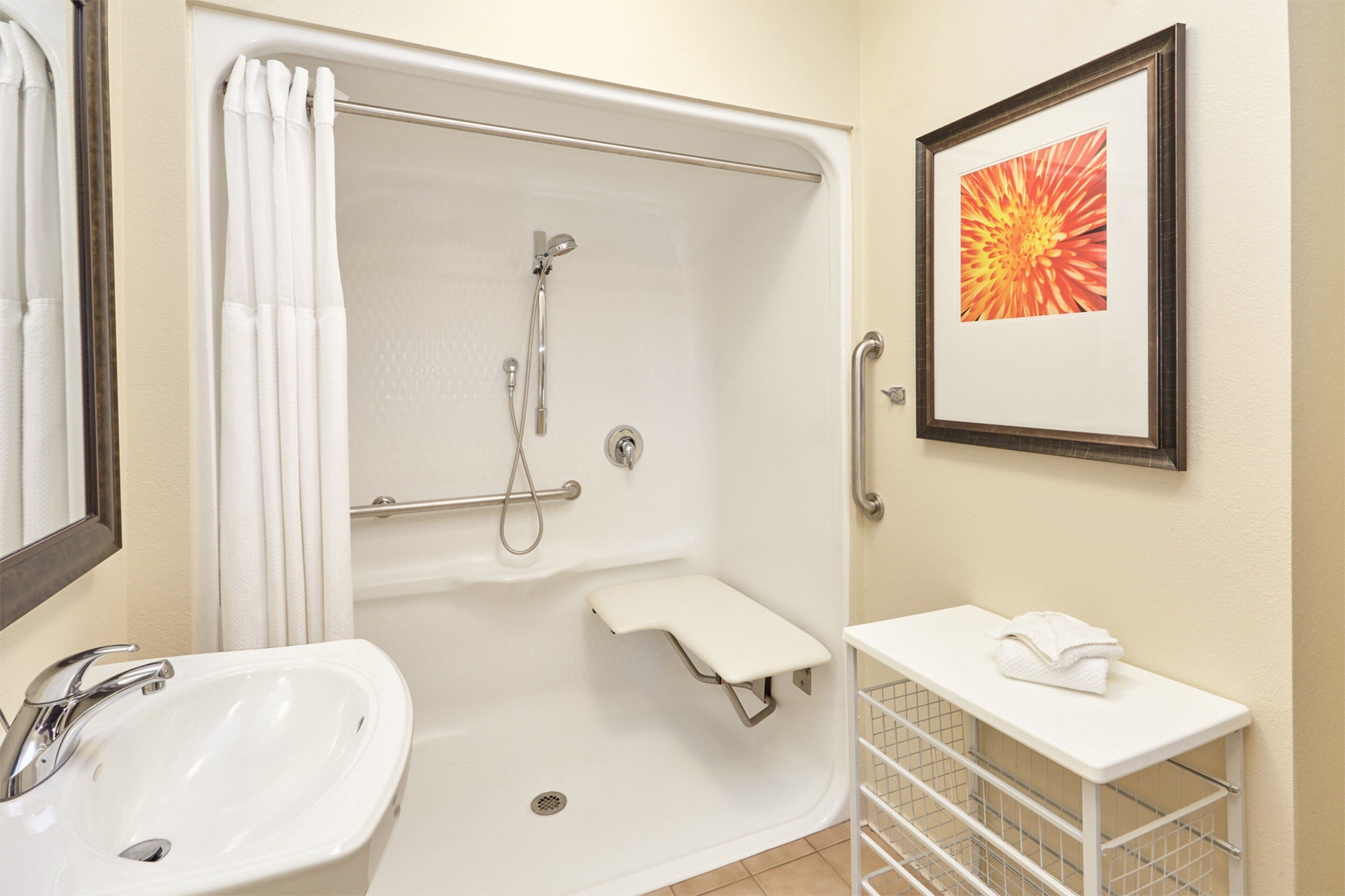 A bathroom with a bathtub, a sink, a shower, a framed picture, and a towel rack.