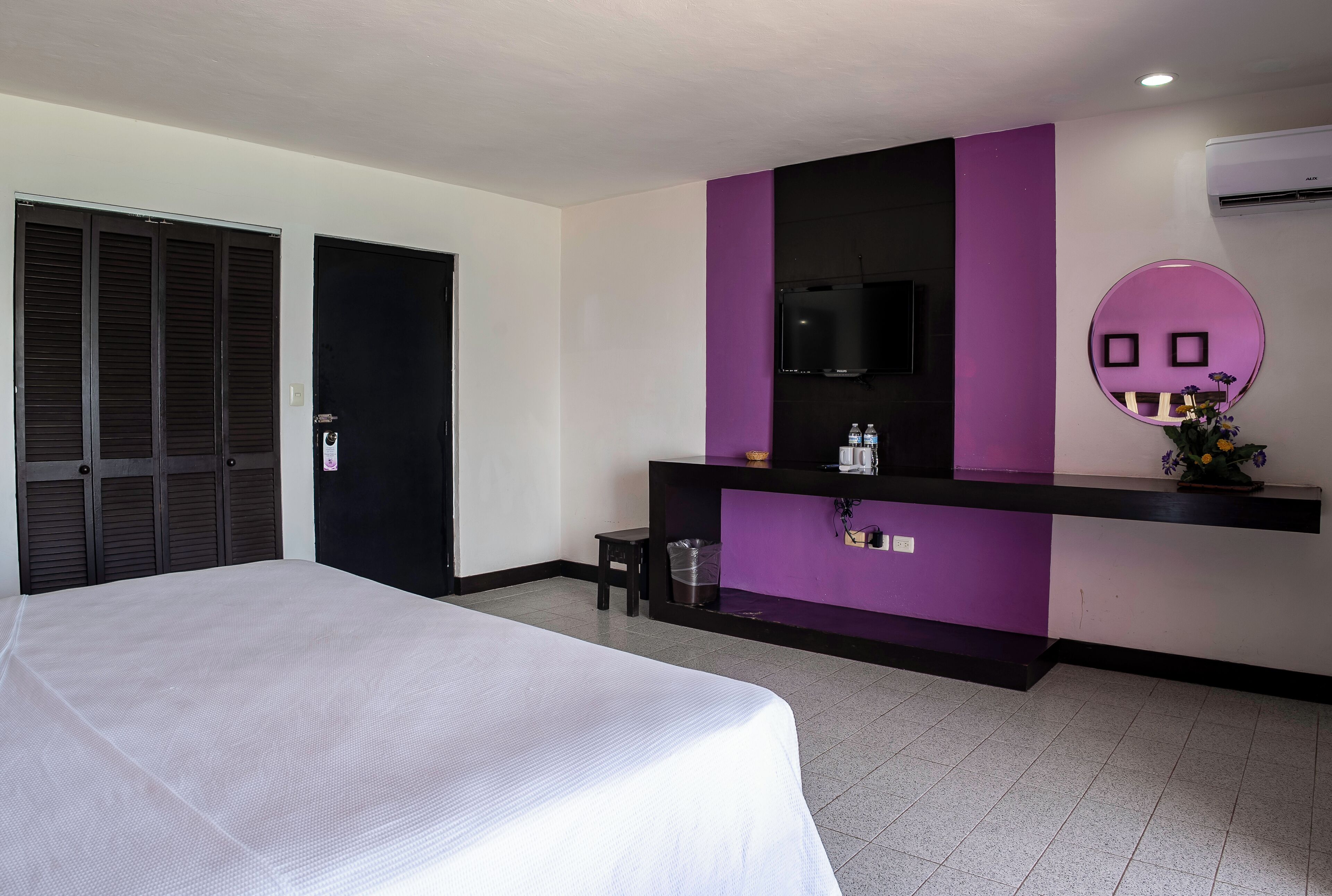 Habitación de hotel con cama, escritorio con espejo y televisor.