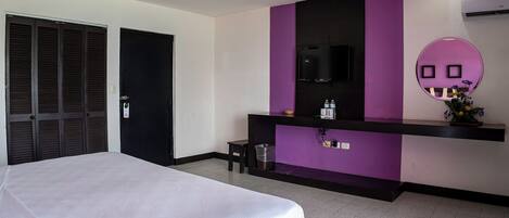 Habitación de hotel con cama, escritorio con espejo y televisor.