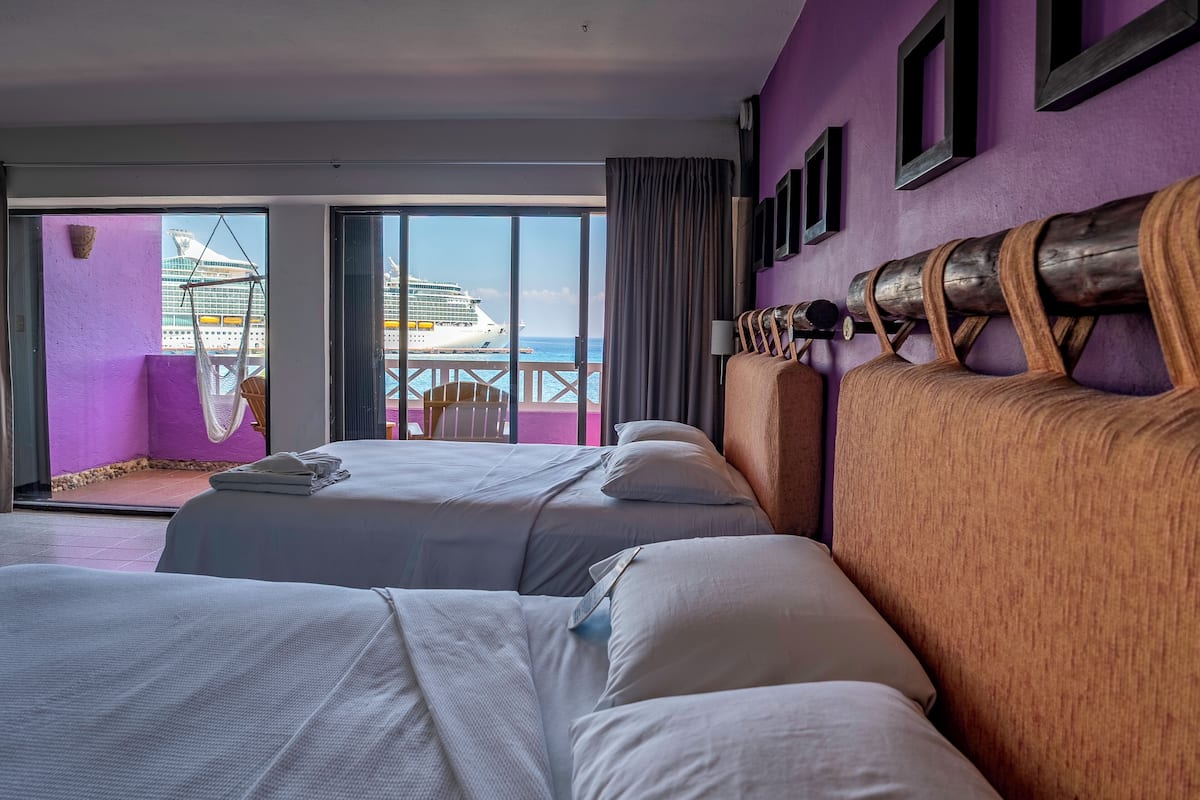 Een hotelkamer met twee bedden, uitzicht op een cruiseschip en een balkon met een stoel.