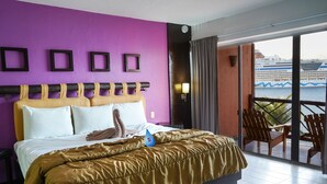 Habitación de hotel con una cama grande, paredes moradas y un balcón con vista a un crucero.