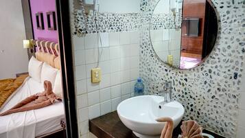 Habitación de hotel con cama, baño con lavamanos, espejo y azulejos decorativos.