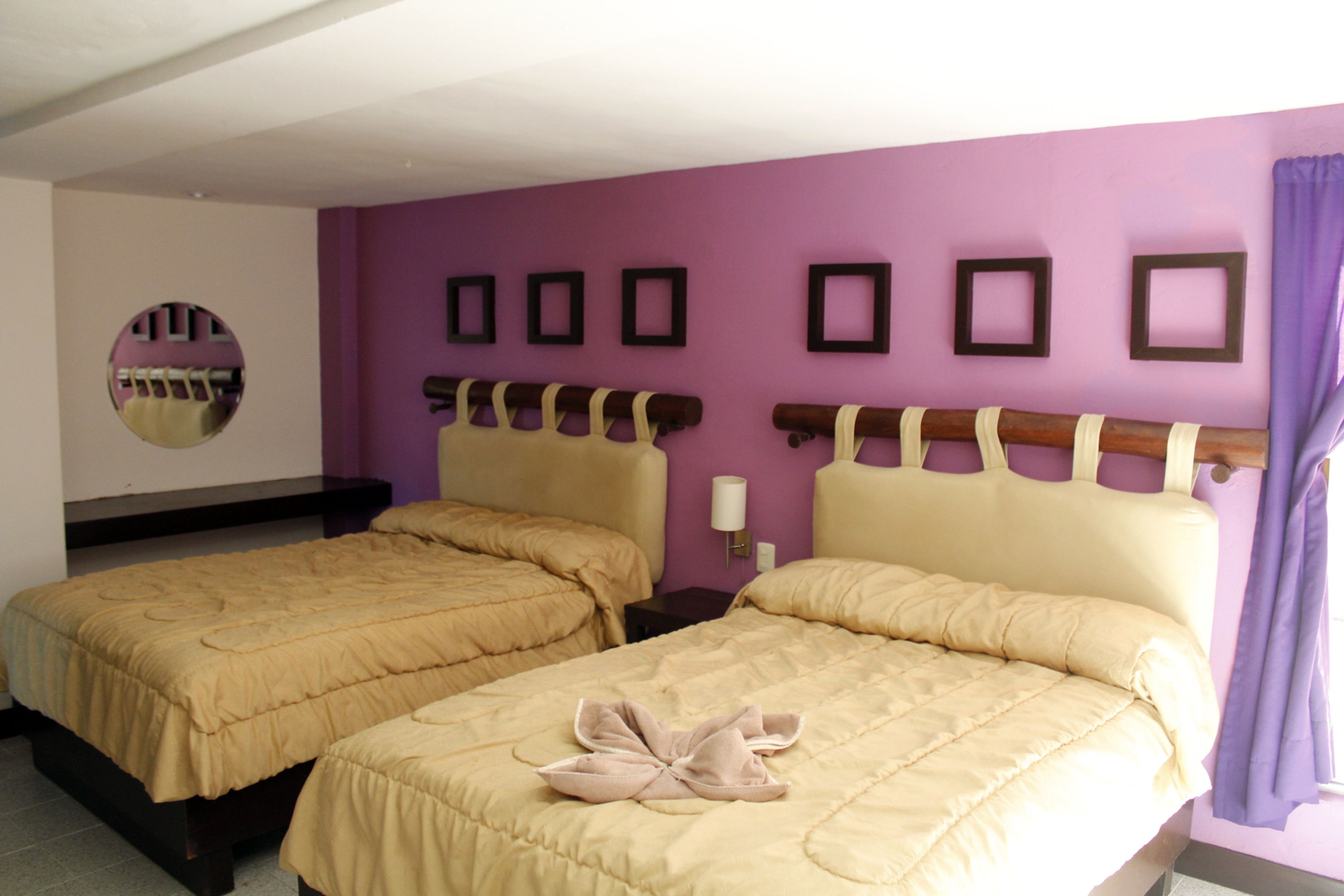 A hotel room with two beds, a purple wall, and a mirror.