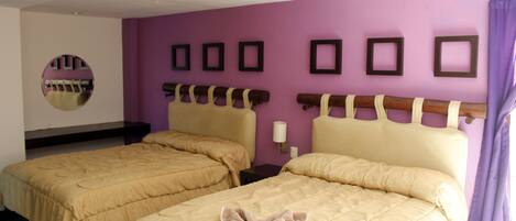 A hotel room with two beds, a purple wall, and a mirror.