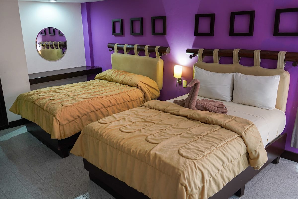 Een tweepersoonsbed met hoofdeinde, nachtkastje en een spiegel aan de muur.