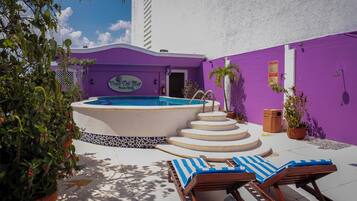 A pool area with a hot tub, lounge chairs, and potted plants.