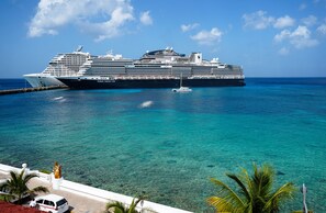 Un gran crucero amarrado en un puerto con aguas turquesas cristalinas y un edificio blanco con una estatua al frente.