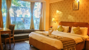 A hotel room with a bed, a desk, and a chair. There is a window with curtains, a lamp, and a framed picture on the wall. - Dee Marks Hotel & Resorts (New Delhi)
