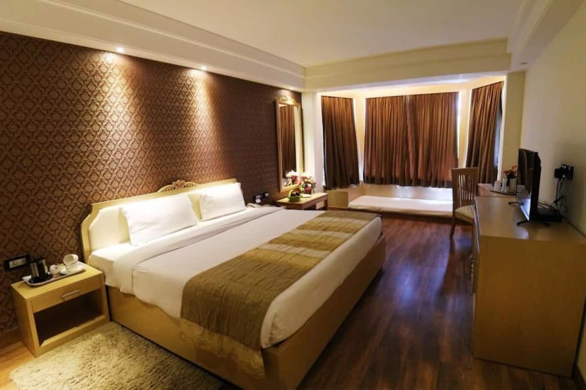 A hotel room with a large bed, a bedside table, a desk, a chair, and a TV.
