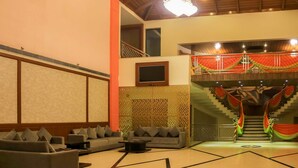 A spacious living area with a sofa set, a coffee table, and a TV mounted on the wall. A staircase with a red and green draped railing leads to an upper level. - Dee Marks Hotel & Resorts (New Delhi)