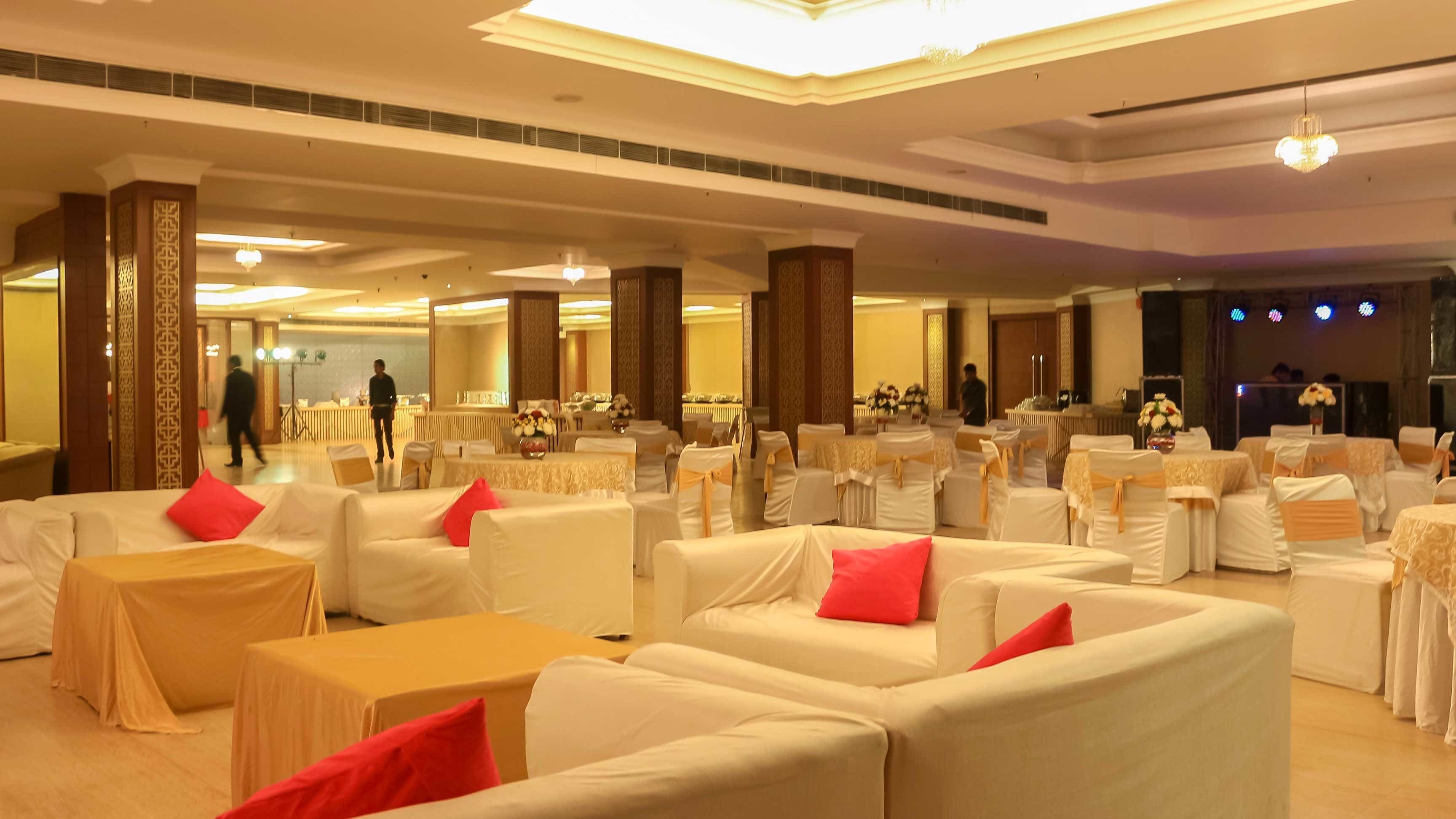 Un amplio salón de banquetes con filas de mesas y sillas blancas, algunas con cojines rojos.