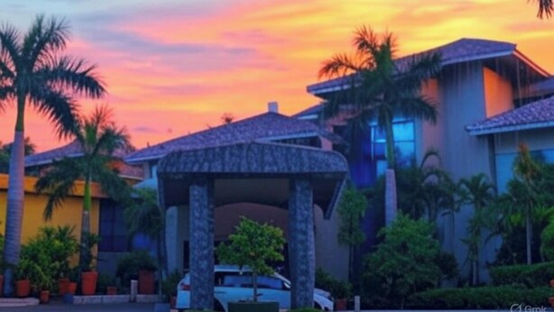 A modern building with a covered entrance, palm trees, and a sunset sky. - Dee Marks Hotel & Resorts (New Delhi)