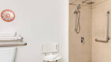 Un baño con ducha, inodoro y una silla blanca.
