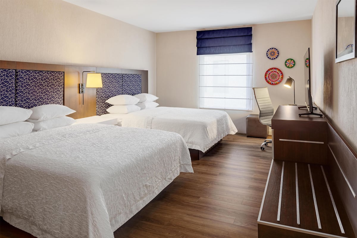 Ein Hotelzimmer mit zwei Betten, einem Schreibtisch, einem Stuhl, einer Lampe und dekorativen Tellern an der Wand.