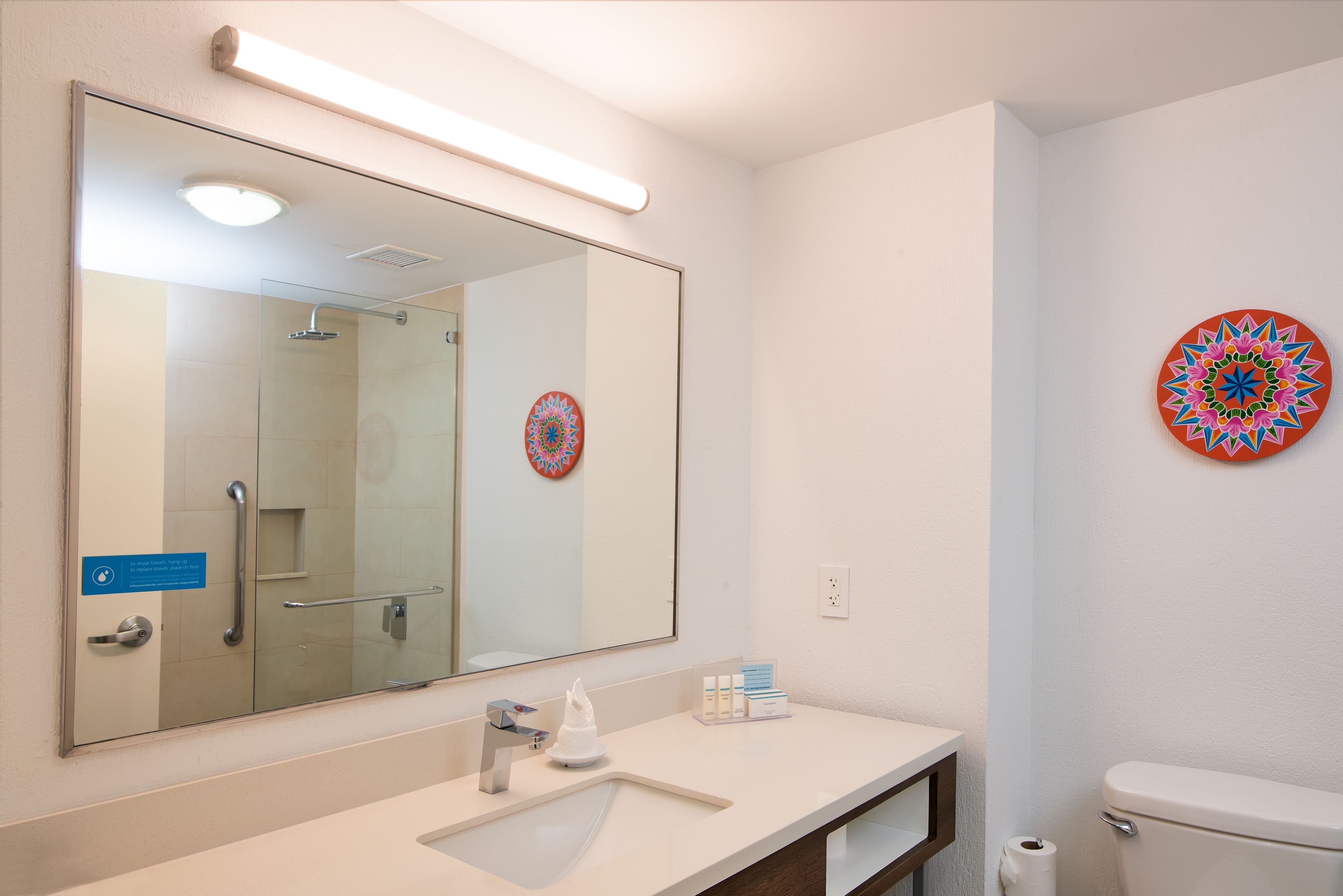 A modern bathroom with a large mirror, a glass shower enclosure, a toilet, and a decorative wall piece.