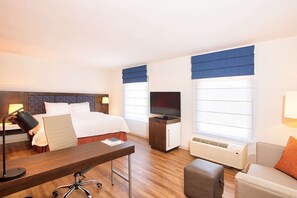 A hotel room with a bed, desk, chair, TV, and a sofa.