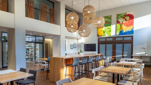 Een modern restaurant met hoge plafonds, houten tafels en stoelen, een bar in het midden en kunstwerken aan de muren.