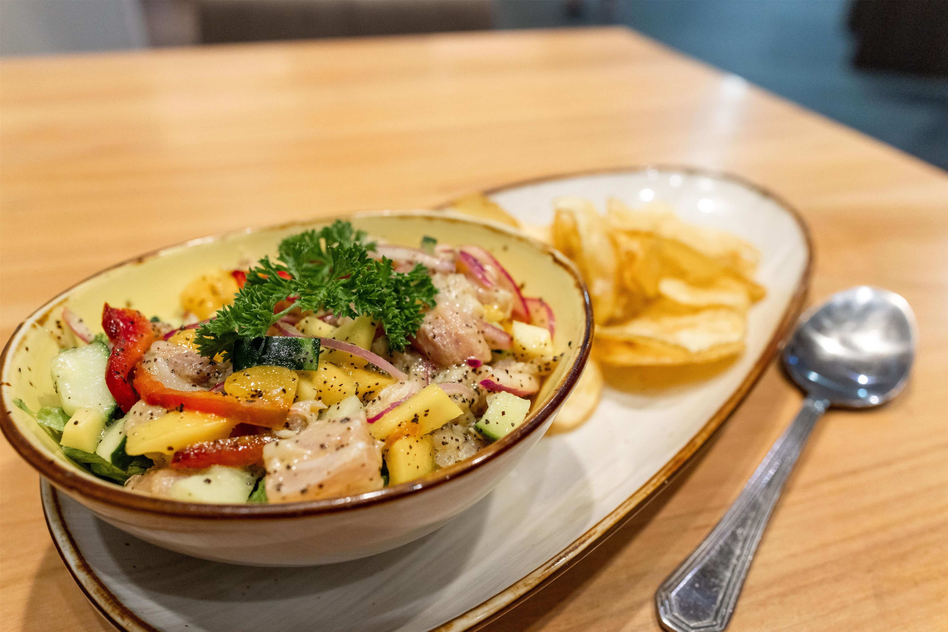 Un tazón de ensalada con diferentes verduras y una cuchara sobre una mesa.