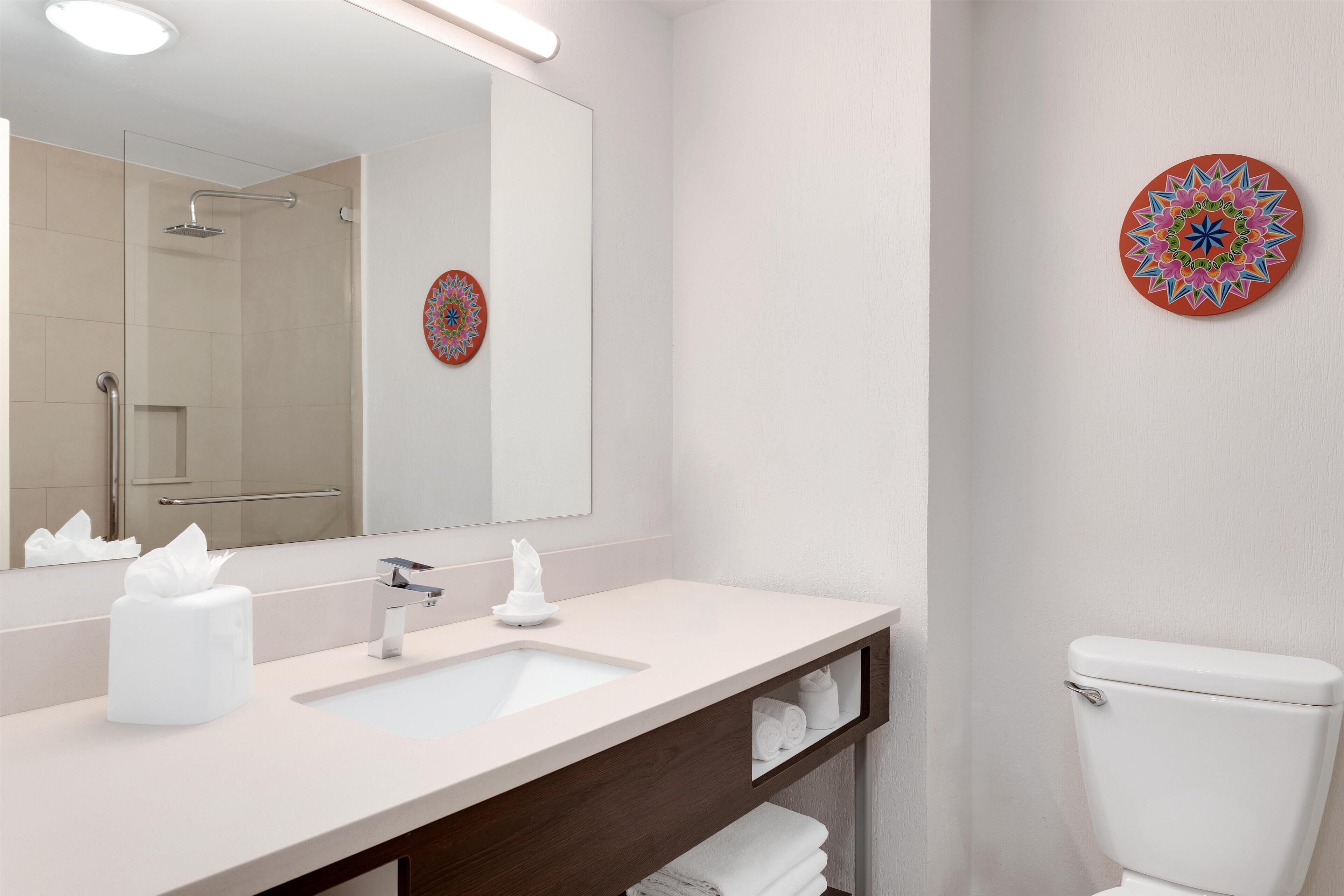 Ein modernes Badezimmer mit einem weißen Waschbecken, Spiegel und WC, sowie dekorativen Wandbildern.