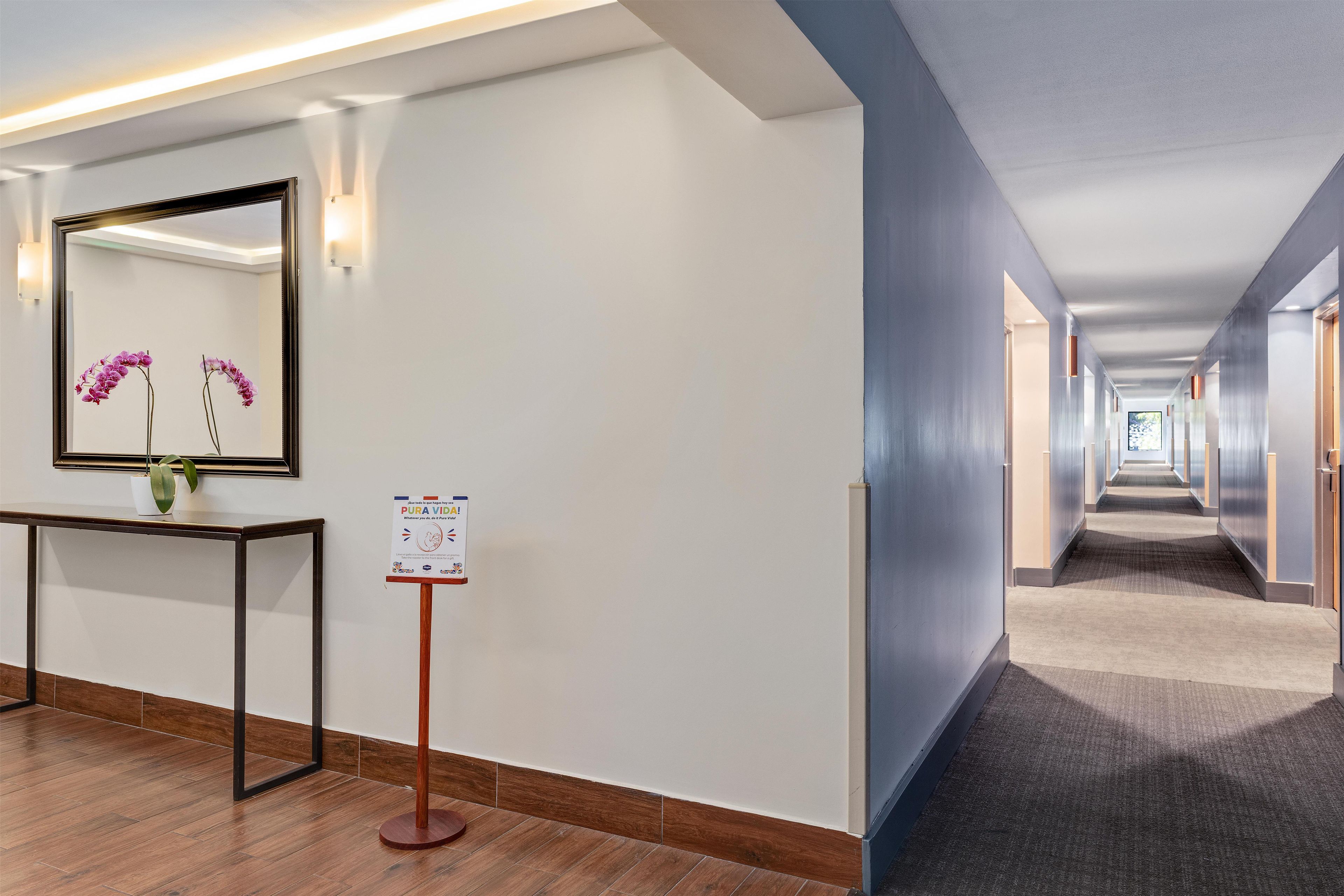 Un pasillo de hotel con piso de madera, una recepción, un espejo en la pared y un letrero.