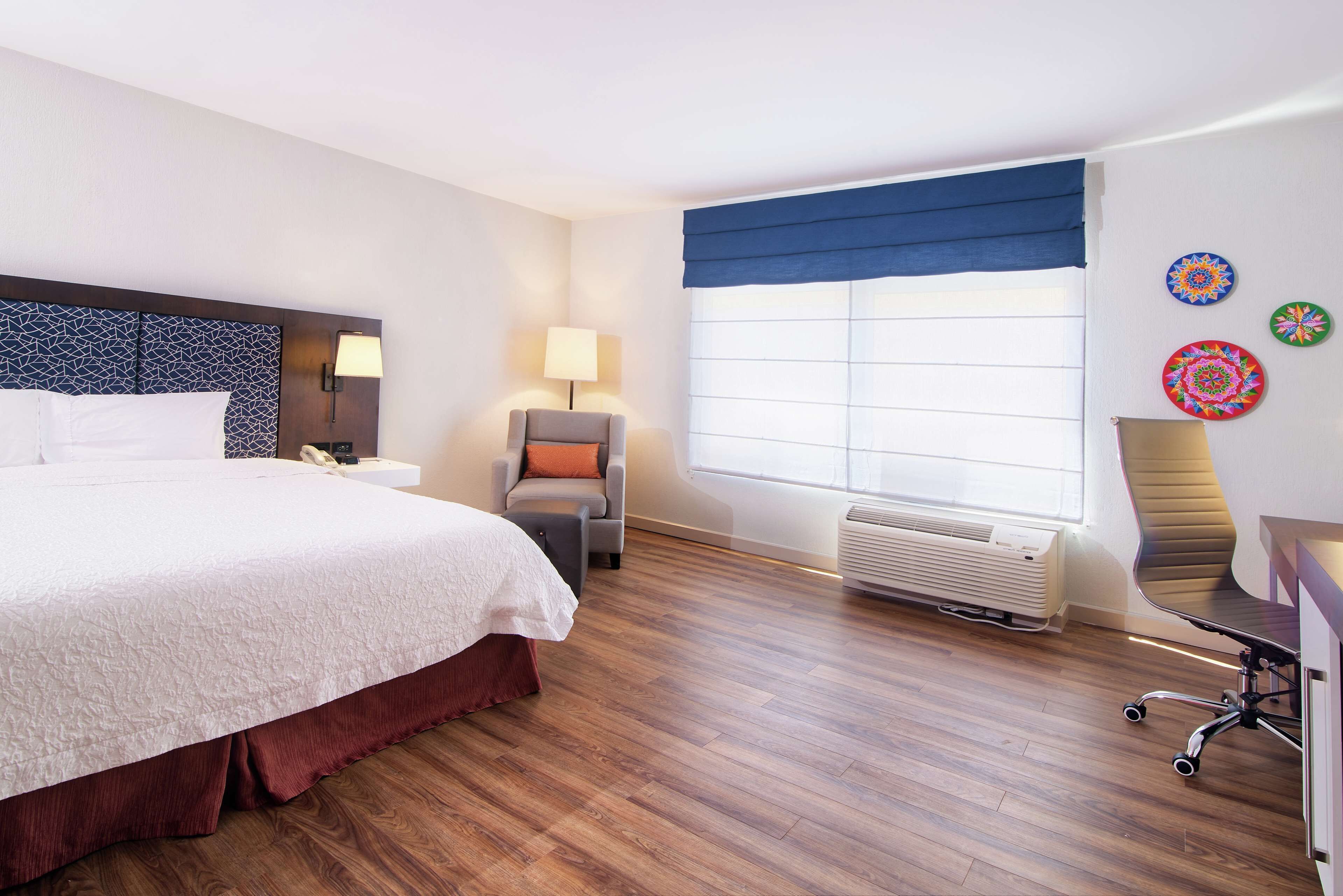 Una habitación de hotel con una cama grande, un escritorio, una silla, una ventana con persianas y paneles decorativos en la pared.