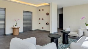 Een moderne lobby met een zithoek, een receptiebalie, een inbouwlift en decoratieve wandkunst.